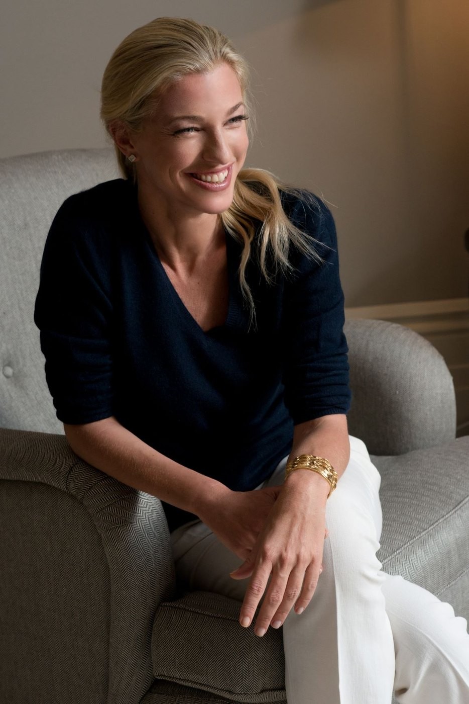 Nicole Brachetti Peretti seated on a sofa in a navy top, smiling in soft daylight